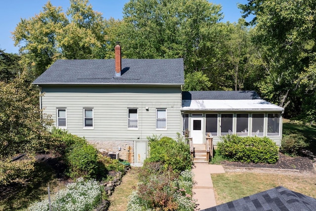 exterior space featuring a sunroom, roof with shingles, and a chimney