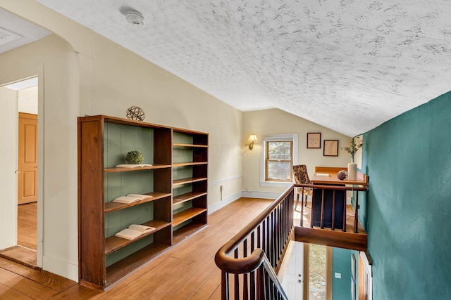 corridor featuring lofted ceiling, a textured ceiling, arched walkways, an upstairs landing, and wood-type flooring