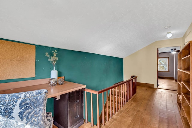 corridor featuring hardwood / wood-style floors, vaulted ceiling, a textured ceiling, an upstairs landing, and baseboards