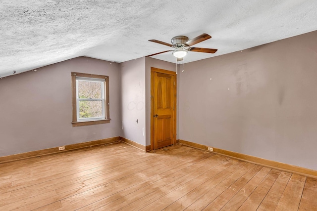 interior space with a textured ceiling, ceiling fan, lofted ceiling, light wood-style flooring, and baseboards