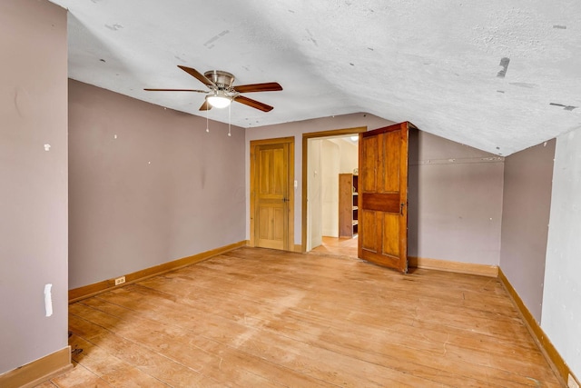 interior space with lofted ceiling, light wood finished floors, a textured ceiling, and baseboards