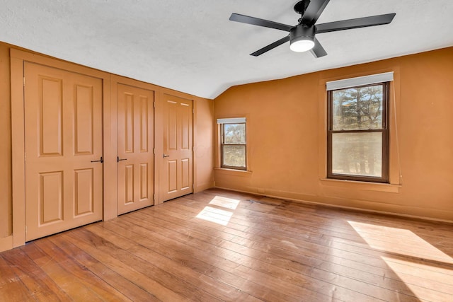 unfurnished bedroom featuring lofted ceiling, a textured ceiling, wood-type flooring, and baseboards