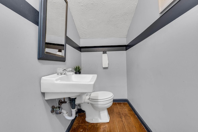 bathroom featuring baseboards, toilet, hardwood / wood-style flooring, a textured ceiling, and a sink