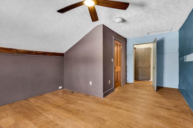 additional living space featuring lofted ceiling, a textured ceiling, visible vents, light wood-style floors, and attic access