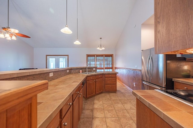 kitchen with stainless steel fridge, ceiling fan with notable chandelier, vaulted ceiling, sink, and hanging light fixtures