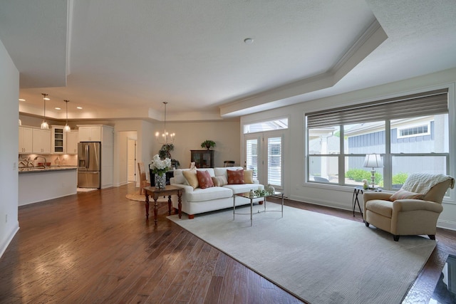 living room with dark hardwood / wood-style flooring, a raised ceiling, crown molding, sink, and a notable chandelier