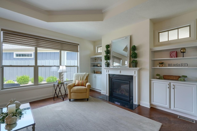 sitting room featuring dark hardwood / wood-style floors, a raised ceiling, crown molding, and a wealth of natural light