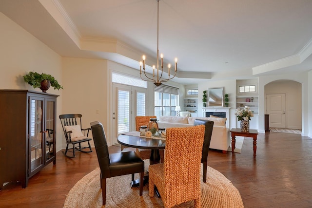 dining area with dark hardwood / wood-style floors, built in features, ornamental molding, and a notable chandelier