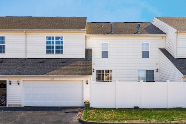 view of property featuring driveway, roof with shingles, an attached garage, and fence