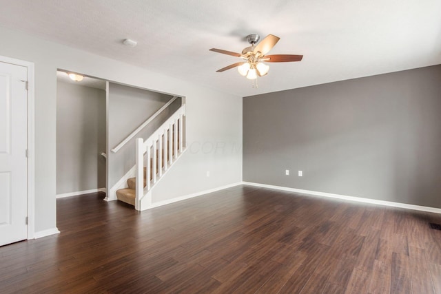 spare room featuring dark wood-style floors, ceiling fan, stairway, and baseboards