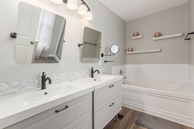 bathroom with double vanity, a garden tub, a sink, and wood finished floors