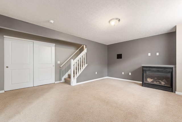 basement with carpet floors, stairs, baseboards, and a glass covered fireplace