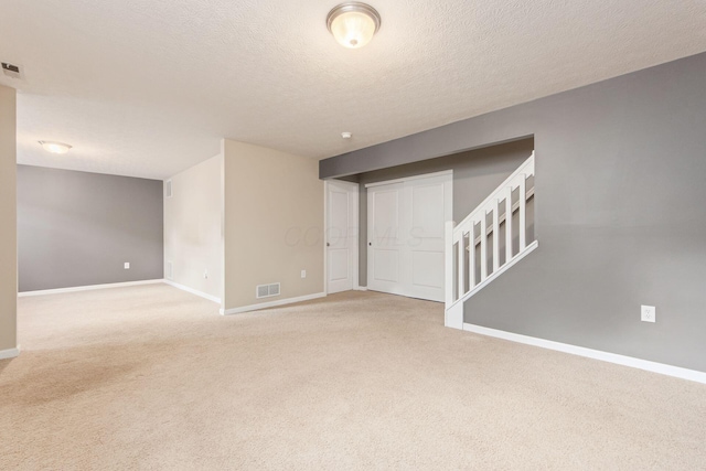 empty room featuring light carpet, stairway, visible vents, and baseboards