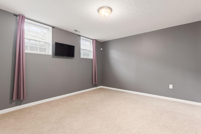 spare room featuring a textured ceiling, carpet floors, visible vents, and baseboards