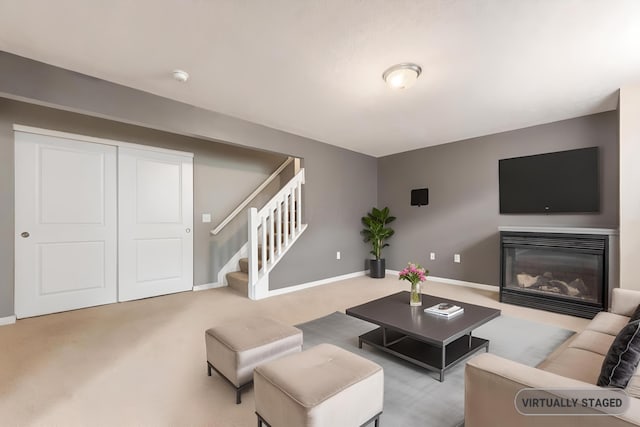 carpeted living room featuring stairs, baseboards, and a glass covered fireplace