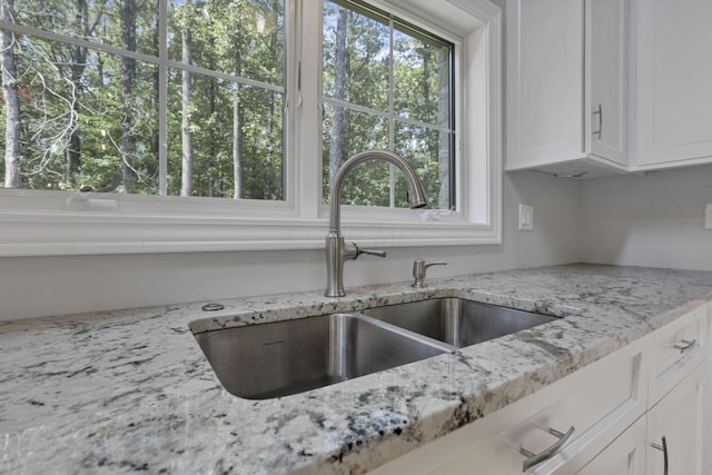 kitchen with white cabinetry, a wealth of natural light, sink, and light stone counters