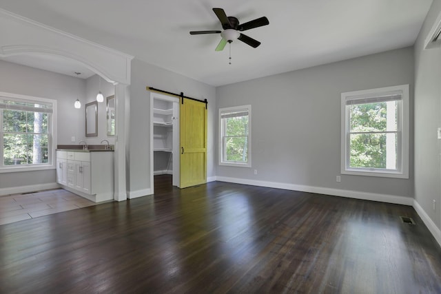 interior space with a barn door, ceiling fan, plenty of natural light, and dark wood-type flooring