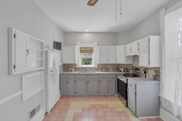 kitchen featuring gray cabinetry, white refrigerator with ice dispenser, stainless steel range with electric cooktop, sink, and tasteful backsplash