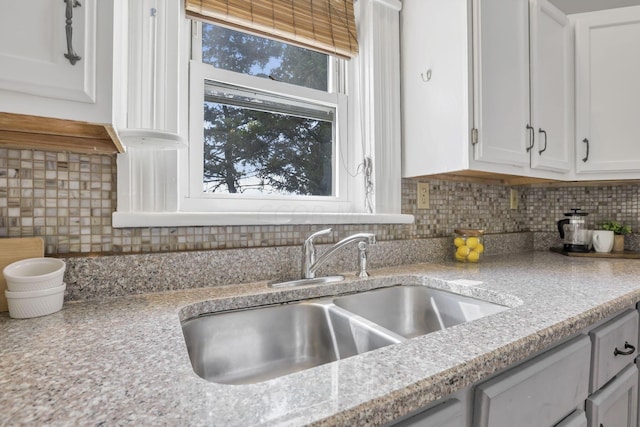 kitchen featuring white cabinets, backsplash, light stone counters, and sink