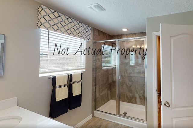 bathroom with a textured ceiling, vanity, wood-type flooring, and a shower with door