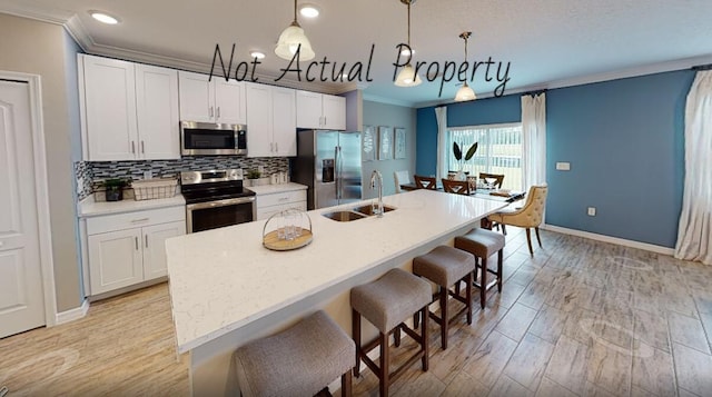 kitchen featuring stainless steel appliances, sink, a center island with sink, white cabinetry, and hanging light fixtures