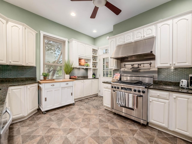 kitchen featuring high end stove, white cabinetry, dark stone countertops, and backsplash