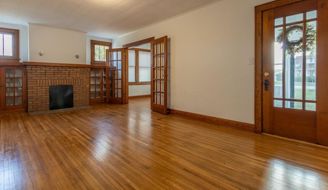 unfurnished living room with a fireplace, wood-type flooring, french doors, and ornamental molding