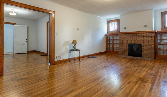 unfurnished living room featuring hardwood / wood-style flooring, crown molding, and a brick fireplace