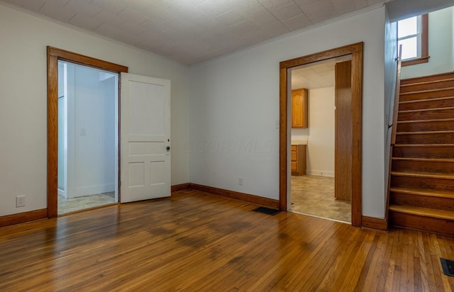 unfurnished bedroom featuring ensuite bath, dark hardwood / wood-style flooring, and ornamental molding