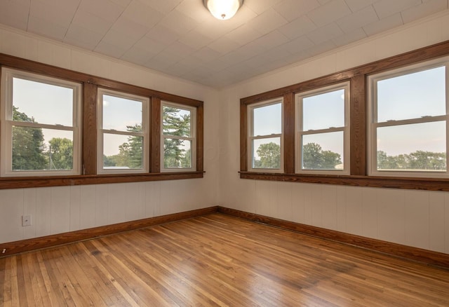 empty room with wood walls, crown molding, and light wood-type flooring