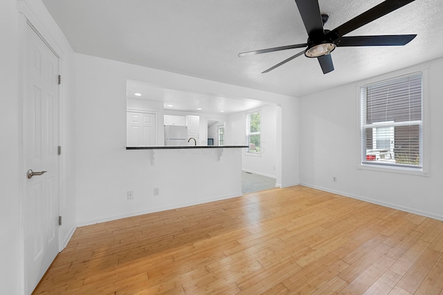 unfurnished living room with ceiling fan, light hardwood / wood-style floors, sink, and a textured ceiling