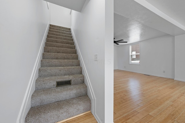 stairway with hardwood / wood-style floors, a textured ceiling, and ceiling fan