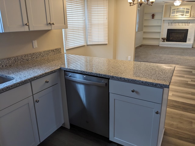 kitchen featuring light stone counters, dark hardwood / wood-style flooring, a brick fireplace, stainless steel dishwasher, and a chandelier