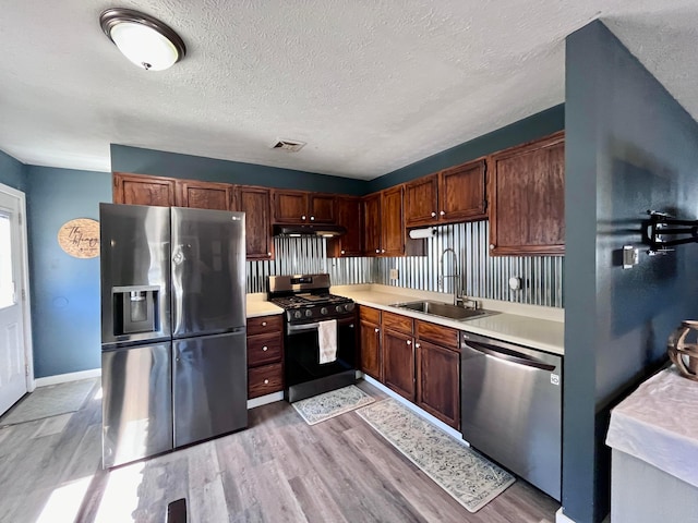 kitchen featuring a textured ceiling, light wood-type flooring, stainless steel appliances, and sink