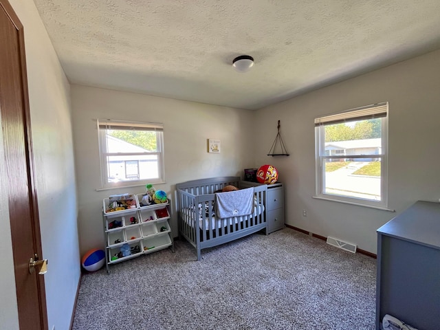 carpeted bedroom featuring a nursery area and a textured ceiling