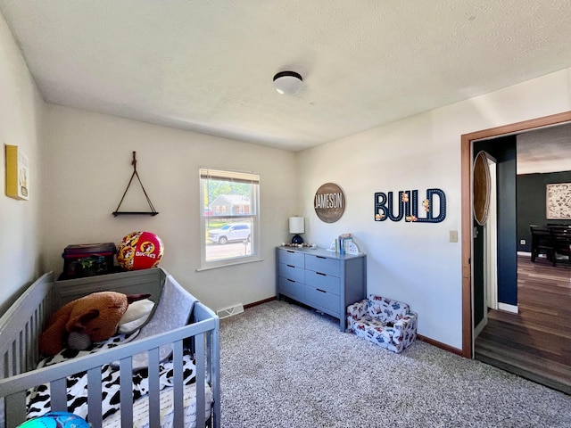 bedroom featuring a crib, a textured ceiling, and carpet floors