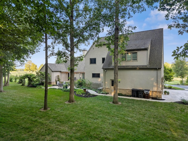 rear view of house featuring a yard, a shingled roof, stone siding, and stucco siding