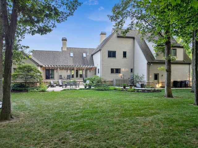 rear view of house with a yard, a chimney, a patio area, and stucco siding