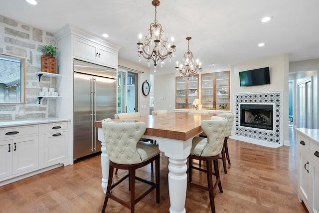 dining area featuring recessed lighting, light wood-style flooring, a tiled fireplace, and a notable chandelier