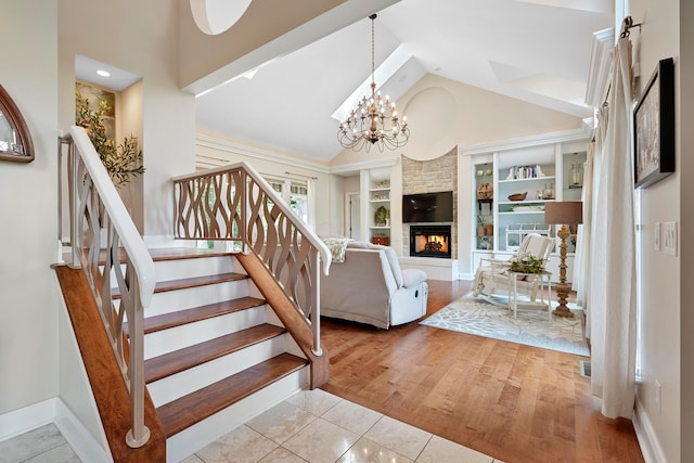 staircase with built in features, a large fireplace, baseboards, high vaulted ceiling, and a notable chandelier