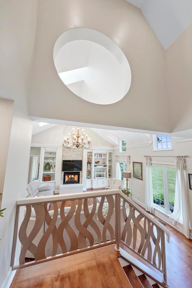 interior space with built in shelves, wood finished floors, high vaulted ceiling, a notable chandelier, and a glass covered fireplace