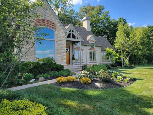 view of front of home featuring a chimney, a front lawn, a shingled roof, stone siding, and stucco siding