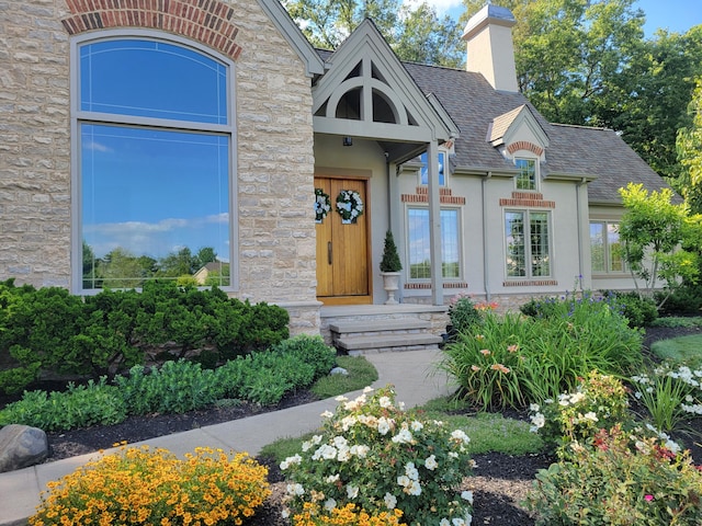 view of exterior entry featuring a chimney, a shingled roof, stone siding, and stucco siding