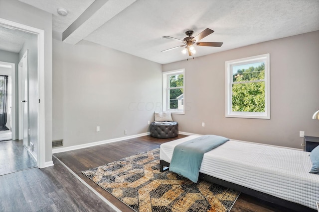 bedroom with beam ceiling, a textured ceiling, dark hardwood / wood-style floors, and ceiling fan