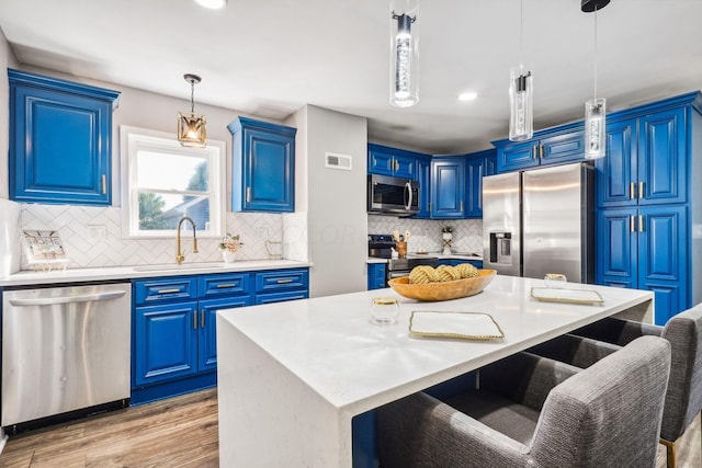 kitchen with blue cabinetry, an island with sink, hanging light fixtures, and appliances with stainless steel finishes