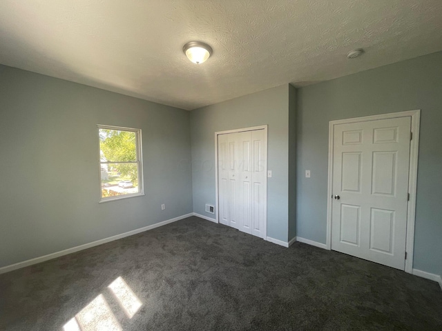 unfurnished bedroom featuring dark colored carpet, a textured ceiling, and a closet