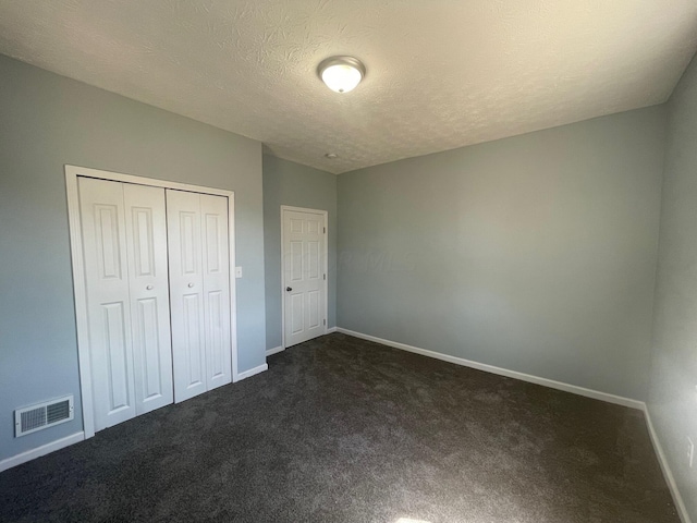 unfurnished bedroom with a textured ceiling, dark carpet, and a closet