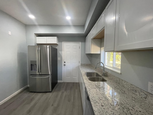 kitchen featuring appliances with stainless steel finishes, light stone counters, sink, hardwood / wood-style flooring, and white cabinetry