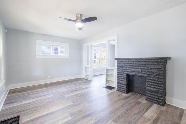 unfurnished living room featuring ceiling fan, a stone fireplace, and wood-type flooring