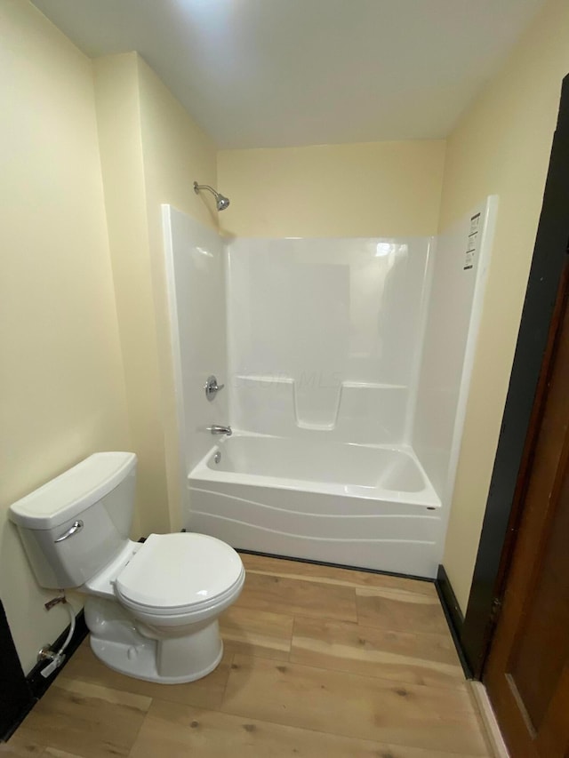 bathroom with wood-type flooring, bathing tub / shower combination, and toilet